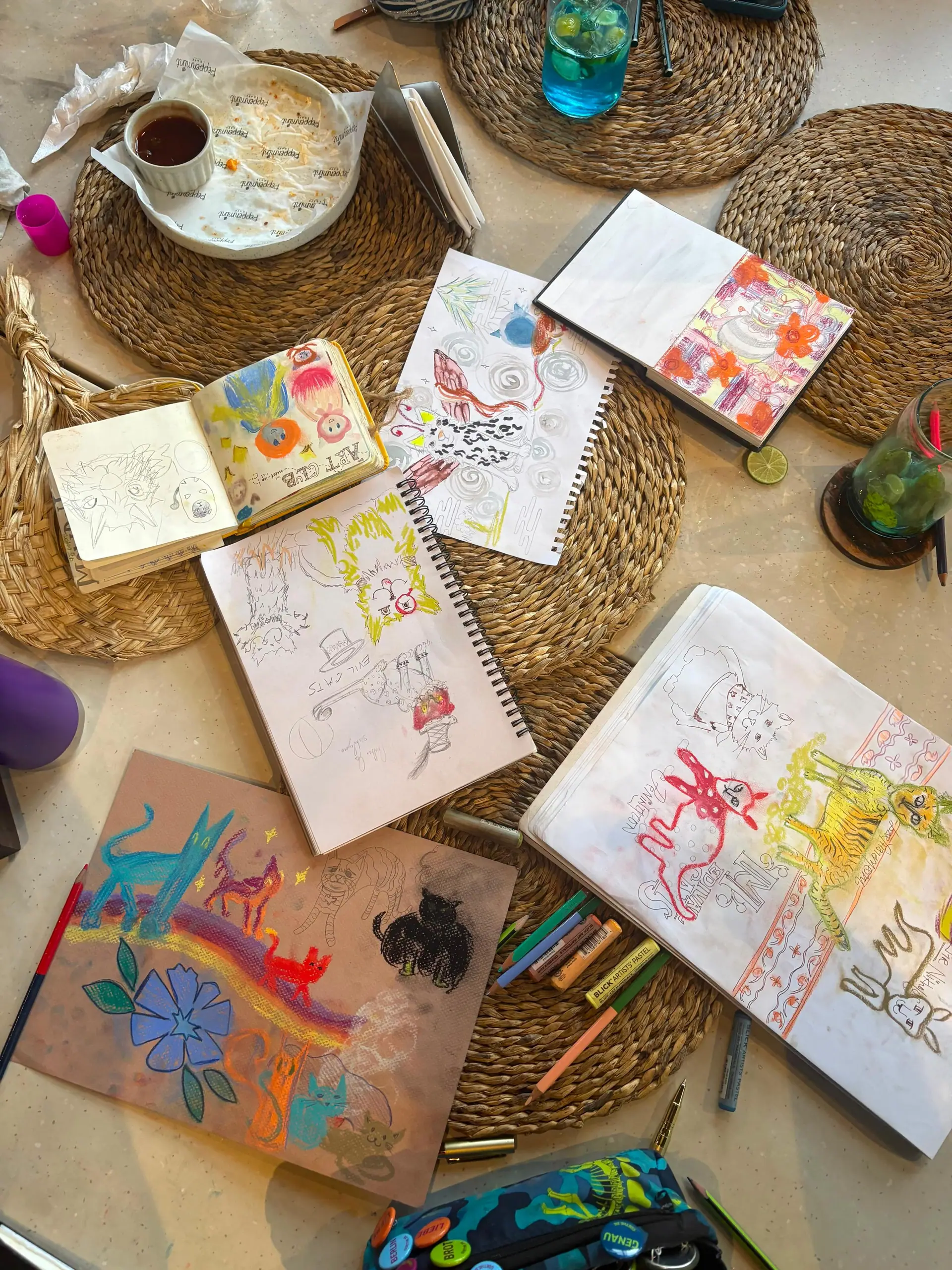 Café table covered in sketchbooks, pastels, and cat doodles